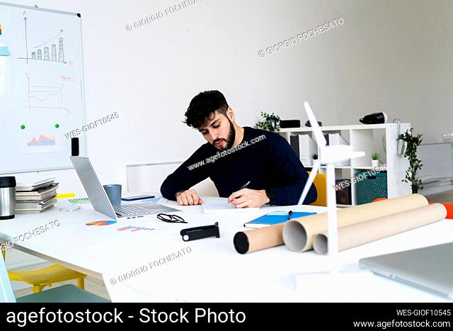 Young businessman writing at desk in creative office