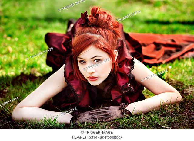 Young female with red hair lying on ground outdoors looking at camera