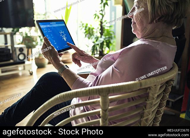 Senior woman checking smart home device while sitting on chair