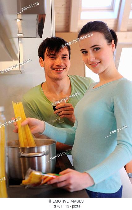 Young couple in kitchen cooking spaghetti and drinking red wine