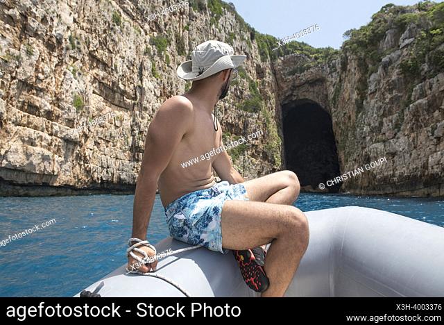 Shirtless man sitting at the bow of a zodiac in front of the Haxhi Ali cave, Peninsula of Karaburun, within the Karaburun-Sazan Marine Parc, Vlore bay, Albania
