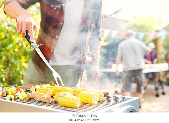 Man barbecuing corn, sausage and vegetable kebabs