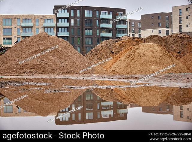 12 December 2023, Hamburg: View of new buildings reflected in a puddle on a construction site in Eidelstedt. The Department for Urban Development and Housing...
