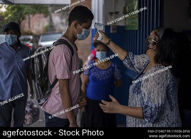 07 April 2021, El Salvador, San Salvador: A teacher measures the body temperature of a student wearing a mouth-nose covering at the entrance of a public school...