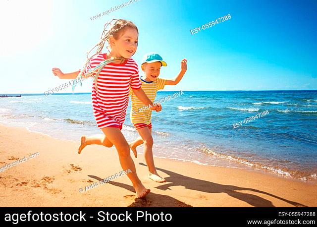Boy and girl playing on the beach on summer holidays. Joyful children in nature with beautiful sea, sand and blue sky. Happy kids on vacations at seaside...