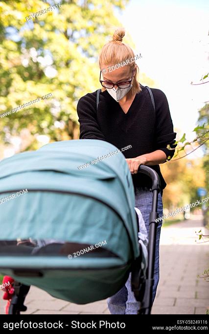 Worried young mom walking on empty street with stroller wearing medical masks to protect her from corona virus. Social distancing life during corona virus...
