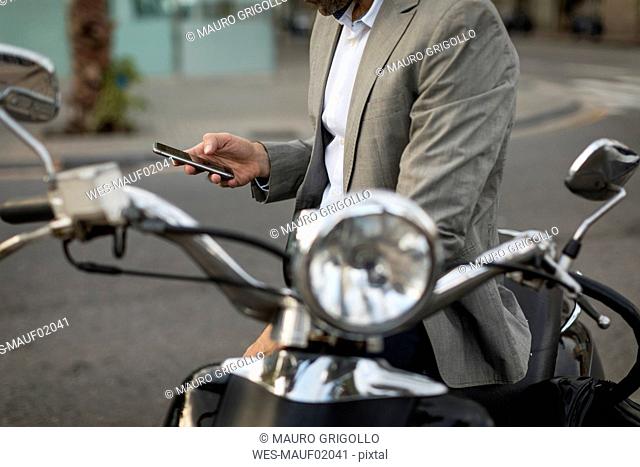 Close-up of businessman on motorscooter checking cell phone