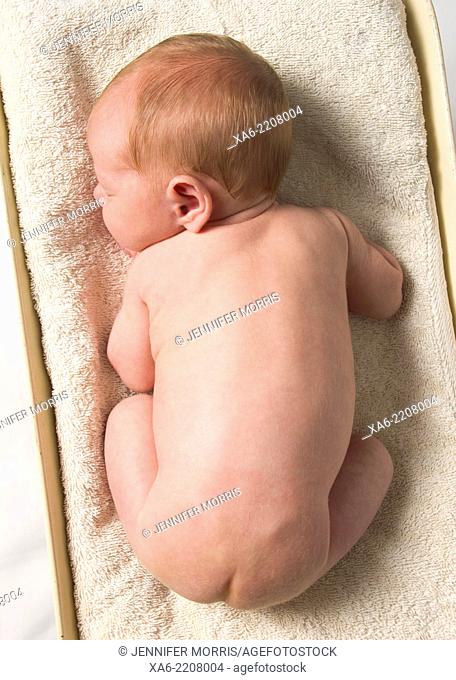 A naked newborn baby lies on a scale