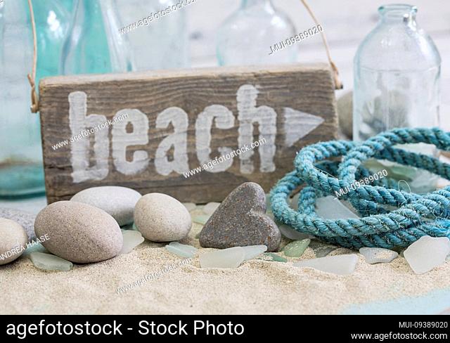 Nautical still life with wooden beach sign, stone heart and old rope