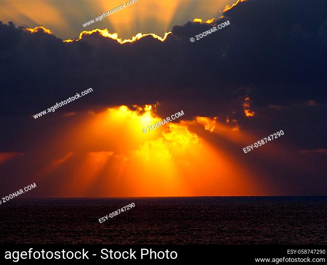 dramatic sunset over the sea with rays of light emerging from dark illuminated clouds over a calm ocean