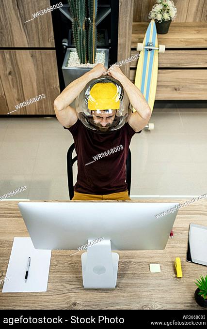 Tensed businessman wearing fishbowl while using computer in modern office