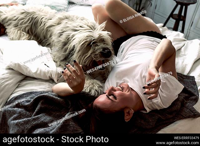 Mature woman lying on bed playing with her dog