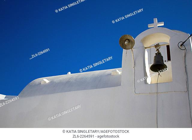 White orthodox church with cross on the top and a bell hanging, against deep blue sky. Pyrgos was built on the top of a hill and was until the early 1800