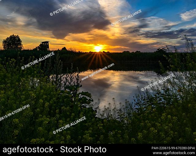 14 June 2022, Brandenburg, Jacobsdorf: Colorful sunset shines over a small lake in the east of the state of Brandenburg. People in Berlin and Brandenburg can...