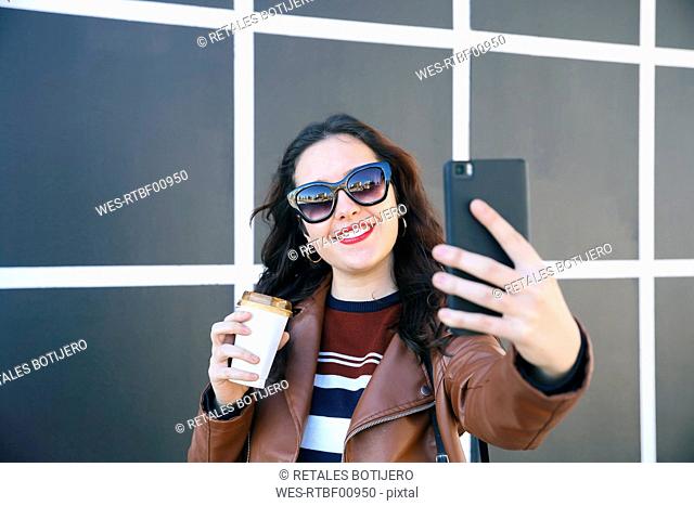 Portrait of smiling young woman with coffee to go taking selfie with smartphone
