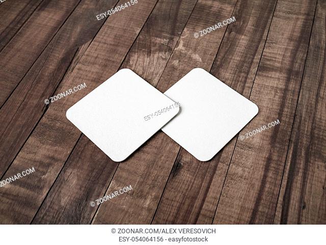 Photo of two blank white square beer coasters vintage wood table background