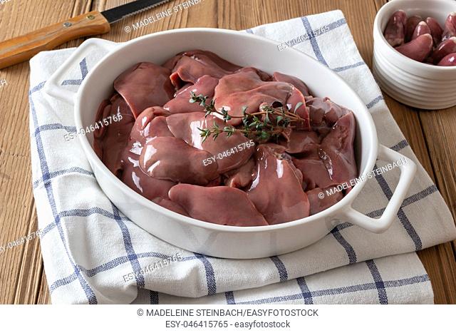 Fresh raw chicken livers in a baking dish, with hearts in the background