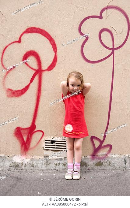 Little girl leaning against wall with flower graffiti, portrait