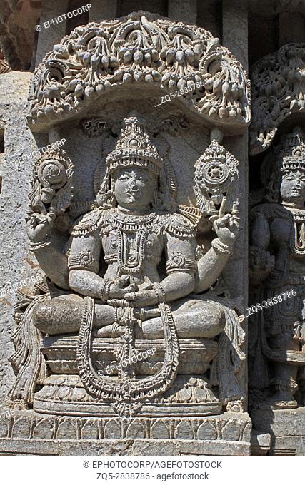 Close up of stone sculpture of(yoga Narayana) lord vishnu sitting in meditative pose, under eves on shrine outer wall in the Chennakesava Temple