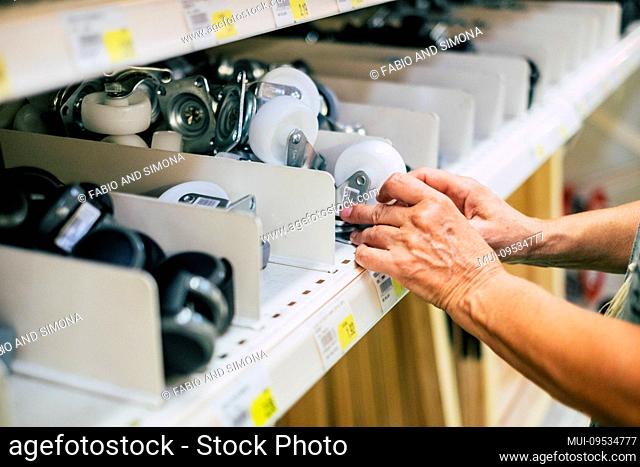 hardware mall people concept - close up of hands taking a wheel from the shelf of the store supermarket or the wall with a lot of wheels - one senior want to...