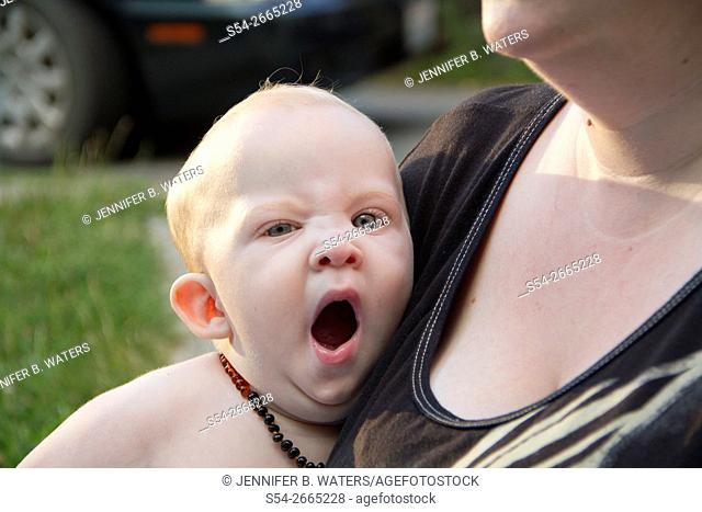 A woman holds her yawning infant son outdoors