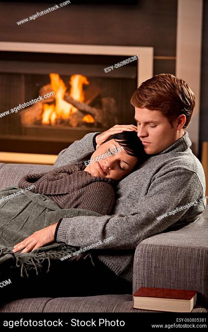 Young couple hugging on sofa in front of fireplace at home, woman sleeping