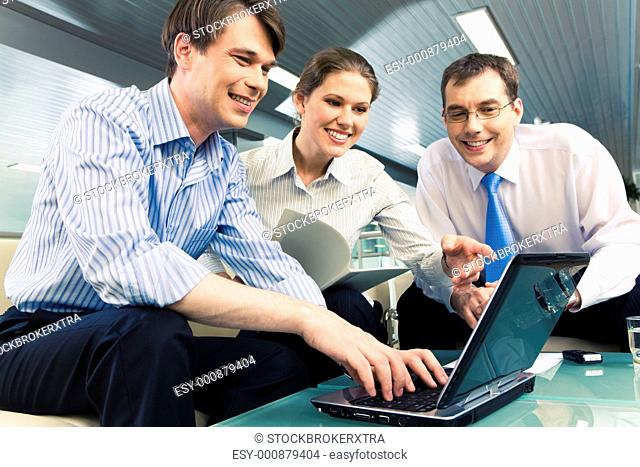 Portrait of young businesswoman holding documents and showing to the monitor of laptop surrounded by two men gathered together around the table with the laptop...