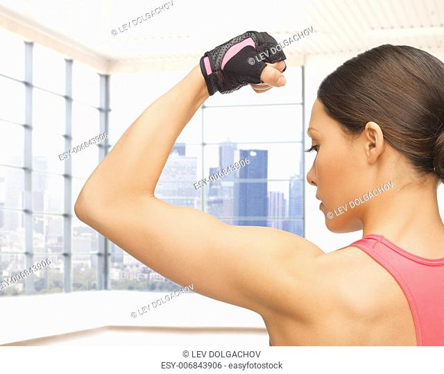 people, fitness, sport and bodybuilding concept - close up of sporty young woman flexing her biceps over gym or home background
