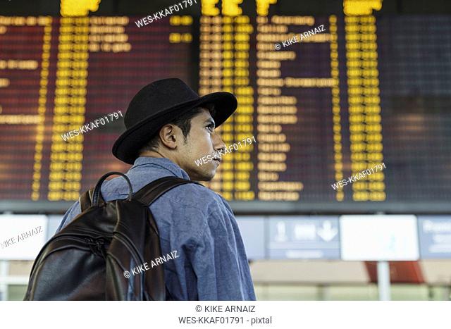 Young man with hat and backpack at arrival departure board at the airport