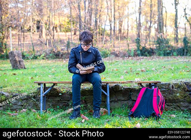 12 year old kid sitting outdoors reads a book, school backpack in the ground-young reader