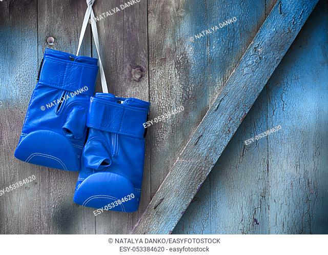 Blue boxing gloves hang on a nail on a wooden shabby wall, empty space on the right