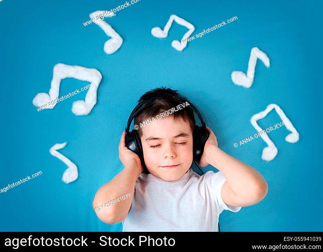 happy little boy on blue blanket background with headphones and musical notes on blue background