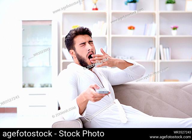 Young man in a bathrobe watching television at home on a sofa couch