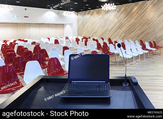 A laptop computer at a podium and rows of chairs in a large room