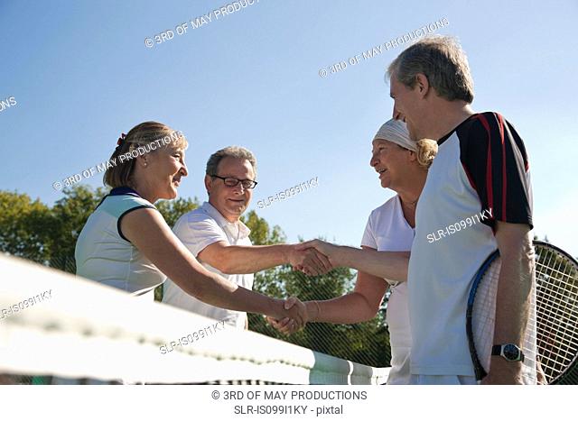 Senior and mature adults shaking hands on tennis court