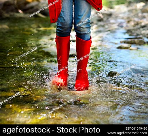 Child wearing red rain boots jumping into a mountain river. Close up