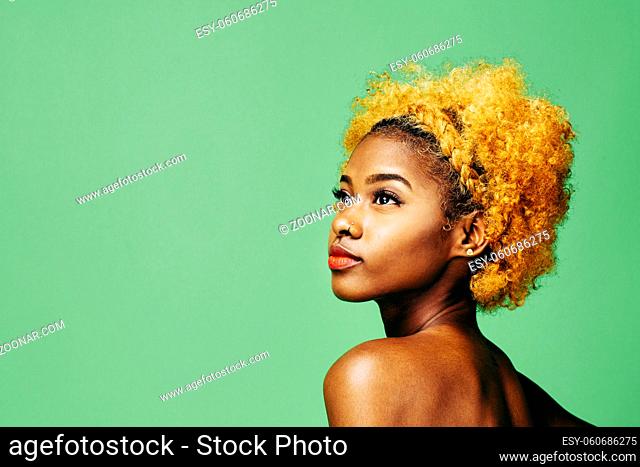Beautiful young girl with bleached curly hair and bare shoulder looking up, in front of a green background
