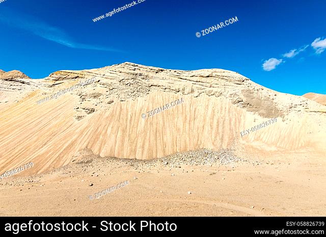 Hills in a sand pit, looks like a mountain. Blue sky and small white clouds in the background