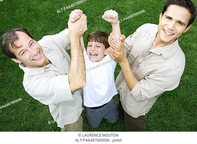 Two men holding up little boy by his arms, all smiling, high angle view