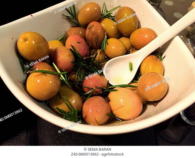 Olives with olive oil and rosemary in white ceramic bowl