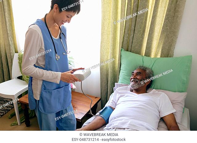 Female nurse checking blood pressure of senior male patient