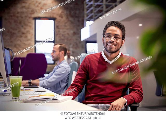 Young man sitting at desk in office, smiling