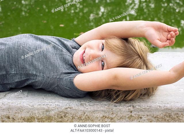 Little girl lying beside pond, smiling, portrait