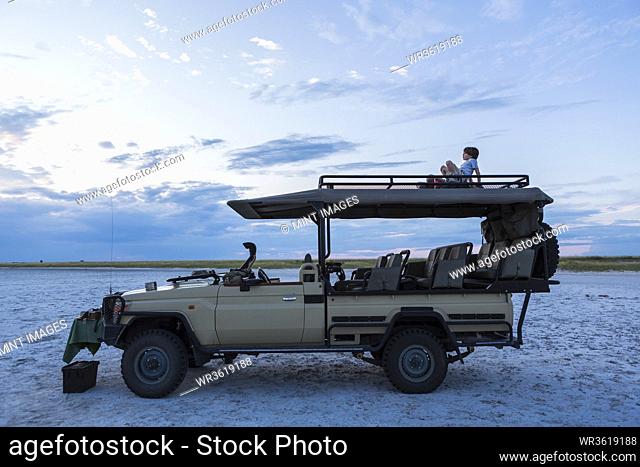 A six year old boy and his teenage sister sitting on top of a safari vehicle at dusk
