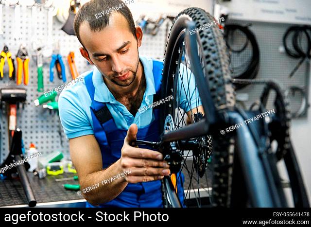 Bicycle assembly in workshop, chain installation. Mechanic in uniform fix problems with cycle, professional bike repairing service