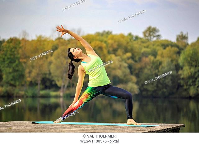 Woman practicing yoga on jetty at a lake