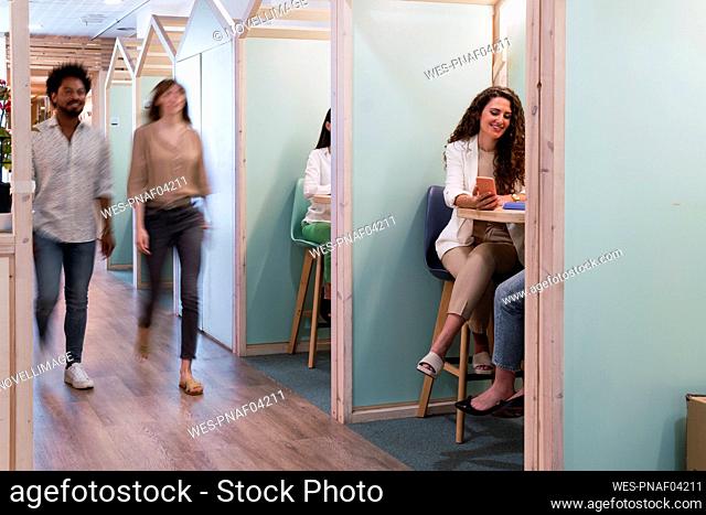 Businesswomen sitting in office cubicles with colleagues passing by