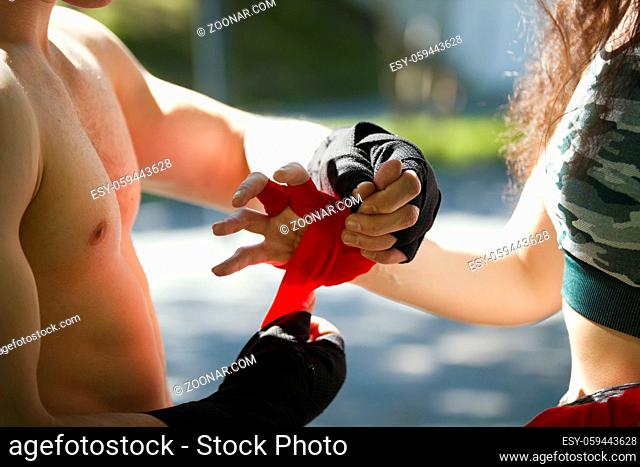 Hands of young man and woman wrapping hands with bandages for workout in summer day, horizontal