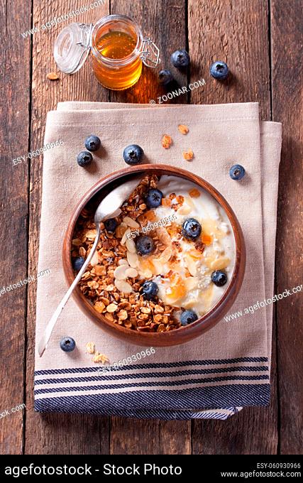 Homemade granola with nuts, candied oranges, fresh blueberries, yogurt and honey in a wooden bowl on a wooden background