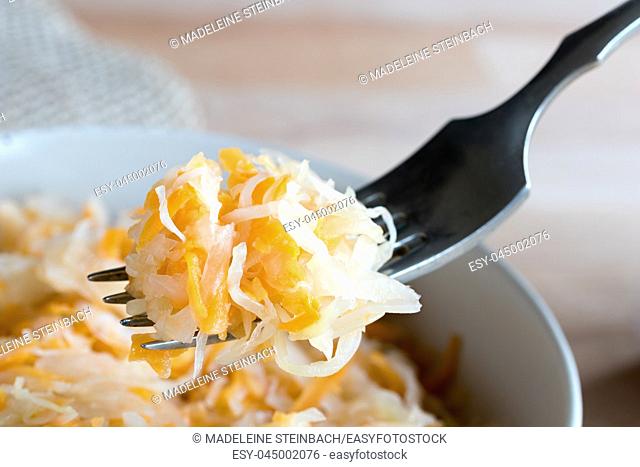 Fermented cabbage and carrots on a fork above a bowl